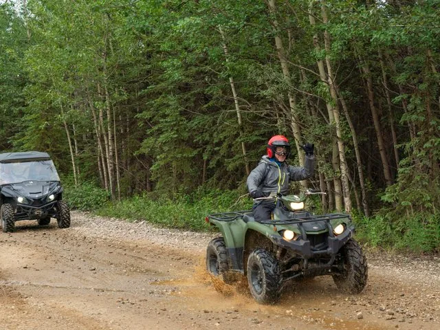 zwei Personen fahren auf Quads auf einem Feldweg durch einen Wald